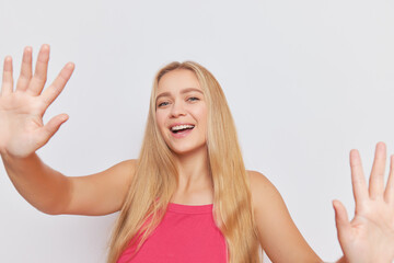 Fototapeta premium Pretty blonde with long hair in pink top smiles isolated over white studio wall holding hands up, nice day concept, copy space