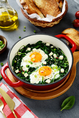 Green shakshuka with fresh spinach, fried eggs and feta cheese cubes, healthy breakfast.