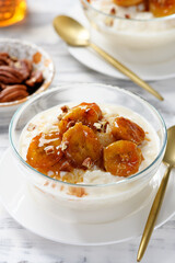 Fresh prepared rice pudding served with caramelized banana, honey and pecan nuts. white wooden background