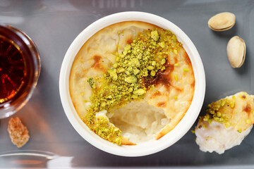 Baked rice pudding- traditional turkish milk dessert, served with pistachio nuts and cup of black tea. top view - 687159382