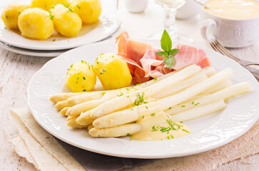 Traditional German white asparagus with boiled potatoes  and juniper ham served as close-up on a classic design plate