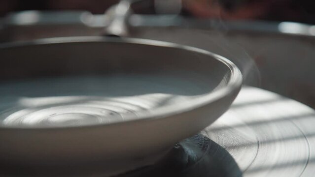Clay product on a potter's wheel. Shot from the side, close-up. A plate made of clay rotates on a potter's wheel, smoke comes from clay - the potter dries the product No people.