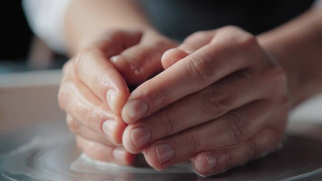 Wet hands of a female potter holding clay on a spinning wheel, close up. Creative process.