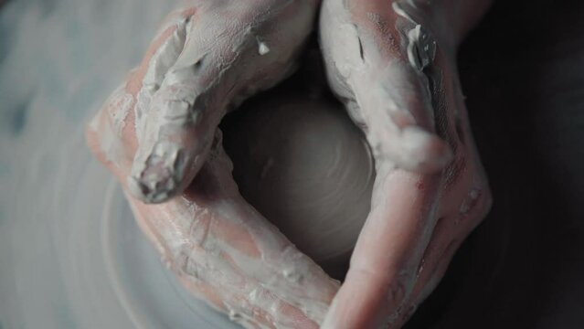 Dirty potter's hands in white clay making a ceramic product on a turning wheel, close up without face. Taken from above