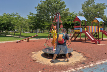 A child on a children's carousel is spun by his father on a playground in a park on a clear sunny...