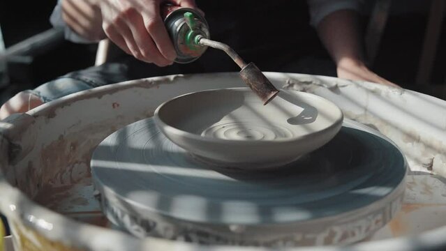 Clay firing. The plate rotates on the potter's wheel the potter dries the product using a gas burner. Natural sunlight in the workshop. Medium plan, no face