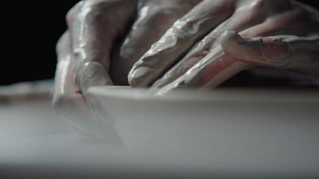 Hands in white clay make a plate on a potter's wheel. Pottery: the process of making handmade tableware. Close up. Handwork.