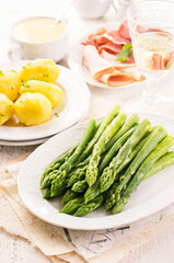 Traditional German green asparagus with boiled potatoes and juniper ham served as close-up on a classic design plate