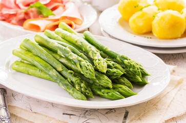 Traditional German green asparagus with boiled potatoes and juniper ham served as close-up on a classic design plate
