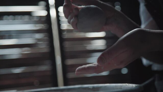A piece of white clay in the hands of a ceramist. Close-up. Filmed at the side: a potter kneads and warms the material for work. Natural lighting in the workshop.