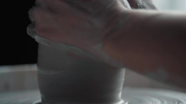 The product made of clay rotates on a potter's wheel, close-up. Creative natural process: the potter makes a glass. Hands in clay make a form.