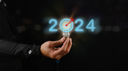 Businessman holding light bulb on black background, concept of setting goals for 2024