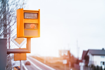 A radar-equipped speed camera monitors the traffic on a road, flashing a yellow light when it catches a car exceeding the speed limit, and using technology to identify the vehicle and enforce the law.