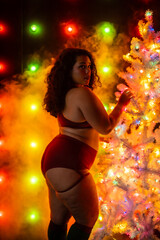 Female in sports bra and short posing in front of red and green christmas themed light wall next to white christmas tree