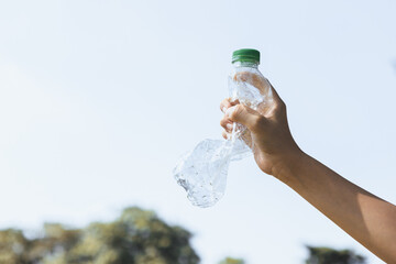 Recyclable plastic bottle held in hand up on sky background. Hand holding plastic waste for recycle reduce and reuse concept to promote clean environment with effective recycling management. Gyre - obrazy, fototapety, plakaty
