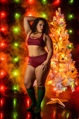Female in sports bra and short posing in front of red and green christmas themed light wall next to white christmas tree
