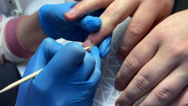 Close-up of a manicure process with blue gloves holding a person's fingertips and a tool applying treatment to the nails