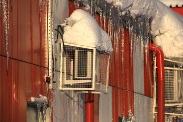 Air conditioning covered with ice and icicles on wall danger for passers, old winter, poor thermal...