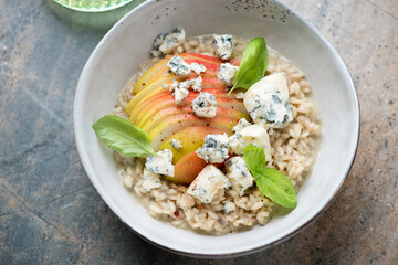 Risotto with pear, blue cheese and fresh basil in a grey bowl, horizontal shot on a beige and grey granite background, elevated view