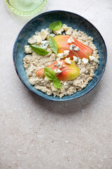 Bowl with pear and blue cheese risotto on a beige stone background, vertical shot with copy space, view from above