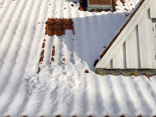 A snowslide down the roof of an old farmhouse makes a rectangular track in the otherwise snow covered tiles