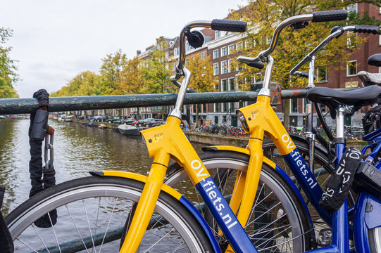 OV-fiets rental bike from NS, the Dutch train company. Yellow and blue bicycle parked on bridge of Amsterdam canal. Close-up. Amsterdam, the Netherlands - October 23, 2023