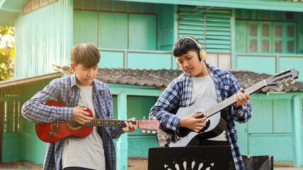 Young Asian boys are playing acoustic guitars in front of a house, soft and selective focus        ...