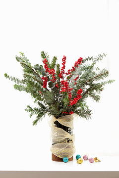 Close-up of fir branches and holly berries in a vase with miniature Christmas baubles on a table