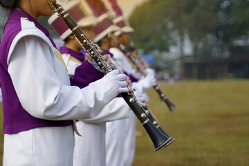 Clarinet players in the high school orchestra in purple and white uniforms play beautifully with...