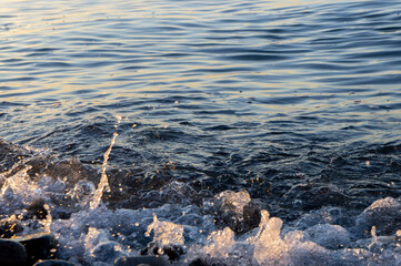 Background: Closeup view of the seawater at sunset. Golden hour. Splashes of water, water bubbles.