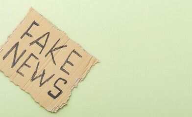 Sign with inscription fake news on a light green background. Top view.