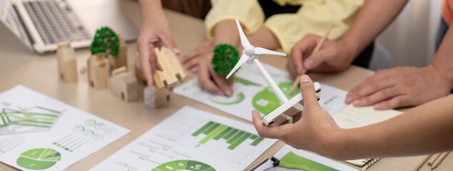Windmill model represented using renewable energy placed during presenting green business on table with wooden block and environmental document scatter around. Closeup. Delineation.