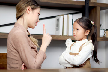 Asian unhappy angry little daughter standing with arms crossed while mother scolding her. Mom...