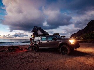 Roaming through the picturesque hawaiian islands, a rugged truck with a tent perched atop traverses sandy beaches, majestic mountains, and clear blue skies, evoking a sense of freedom, adventure, and