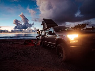 As the sun sets over the golden sand, a fearless woman perches on a ladder atop a truck, her jeep and its wheels ready to take her on a wild journey through the hawaiian islands of kauai and oahu, wi - obrazy, fototapety, plakaty