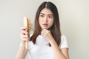 Serious asian young woman holding brush holding comb, hairbrush with fall black hair from scalp...