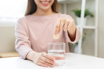 Smile asian young woman putting or dropping effervescent tablet into glass of water, holding pain...