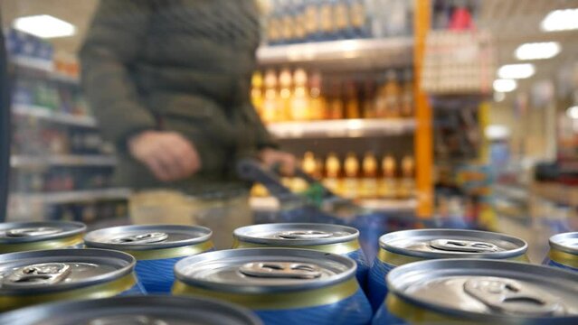A man with a shopping trolley opens the fridge door and takes three cans of beer
