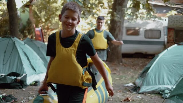 Teenagers in a life jacket at camp carry rubber kayaks ready to ride