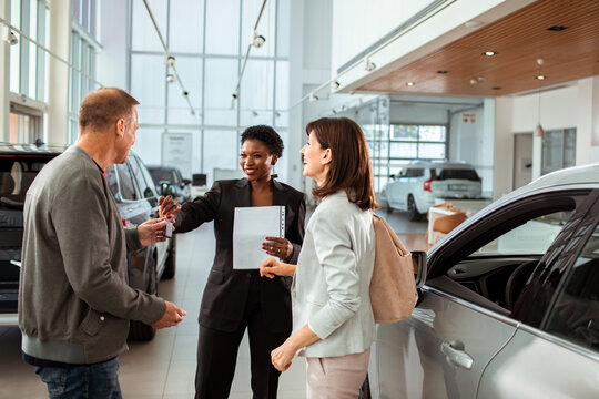 Couple signing paperwork to purchase a new car at dealership with saleswoman