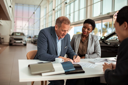 Couple signing paperwork to purchase a new car at dealership with salesman