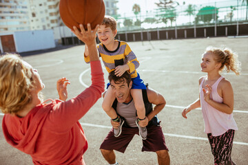 Young family playing basketball together at an outdoor basketball park