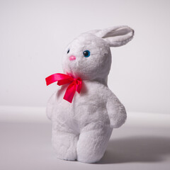 Kid's toy plush hare sitting on a white background. Soft toy for a child. Grey rabbit with a pink nose, isolated on white.