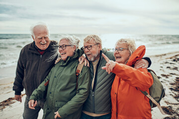 Group of senior friends walking on the beach during winter