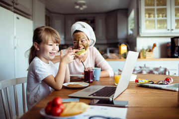 Mother and daughter using laptop during breakfast in the kitchen