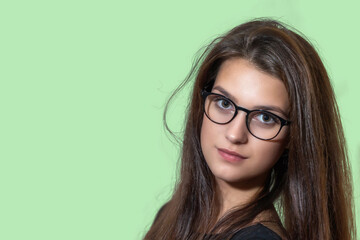 Portrait of long hair girl with glasses posing on the green backgropund. Horizontally. 