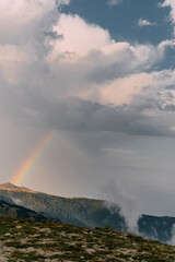 Landscape with a rainbow in a stormy sky among mountains and low clouds