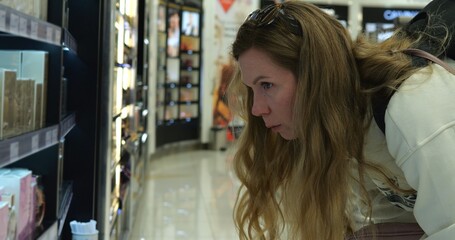 Tourist woman in duty free perfume shop search for specific brand of fragrance. Young female buyer...