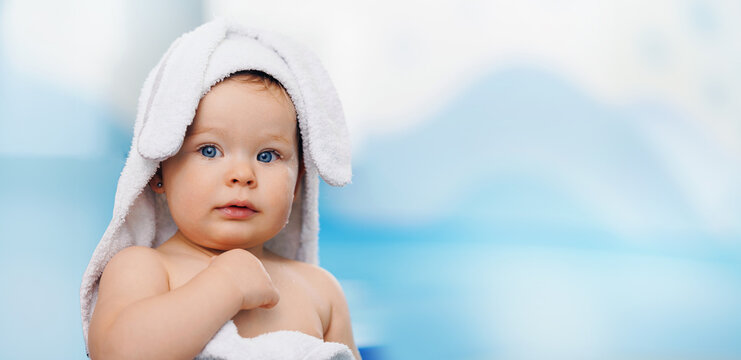 Portrait happy baby girl in white towel with ears after swimming lessons in pool, blur background