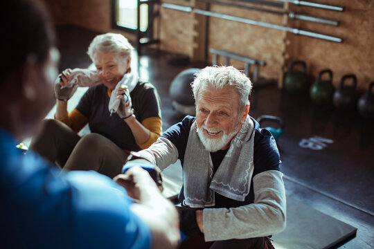 Smiling senior man making fist bump with fitness trainer after gym workout